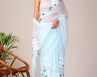 Peut inclure: Un sari bleu clair avec des motifs floraux blancs et des feuilles vertes. Le sari est drapé sur un haut blanc. Le motif floral est répété sur le tissu. Le sari est un vêtement traditionnel.