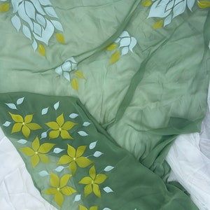 May include: A green sheer fabric with white and yellow floral designs. The fabric is folded in half, with the white flowers on the top half and the yellow flowers on the bottom half.