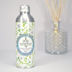 May include: A silver metal bottle with a white label that says "Woodsage & Sea Salt Reed Diffuser Oil" and "Sarah Emily Handmade Candles, Cosmetics & Crafts". The label has a green and white floral pattern. The bottle is 200 ml.
