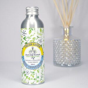 May include: A silver metal bottle with a white label that says "Fresh Linen" and "Reed Diffuser Oil". The label has a yellow circle with a small illustration of a house and the text "Sarah Emily Handmade Candles, Cosmetics & Crafts". The label also has a green and white floral pattern.