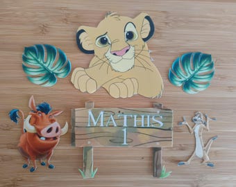 May include: A set of Lion King themed cake toppers featuring Simba, Pumbaa, Timon, and a sign that says "MATHIS 1". The toppers are made of cardstock and are perfect for a first birthday party.
