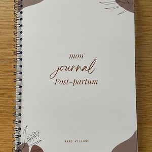May include: A cream-coloured spiral-bound journal with brown text and abstract design elements. The cover reads "mon journal Post-partum" in script. The journal is from "MAMS VILLAGE".
