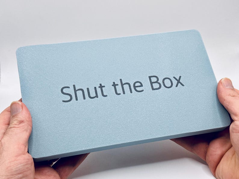 May include: A light blue rectangular box with the text "Shut the Box" printed on the top.
