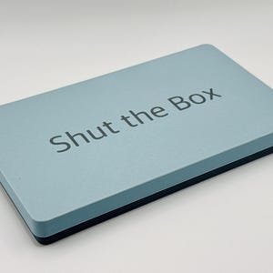 May include: A light blue box with the text "Shut the Box" printed on the top.