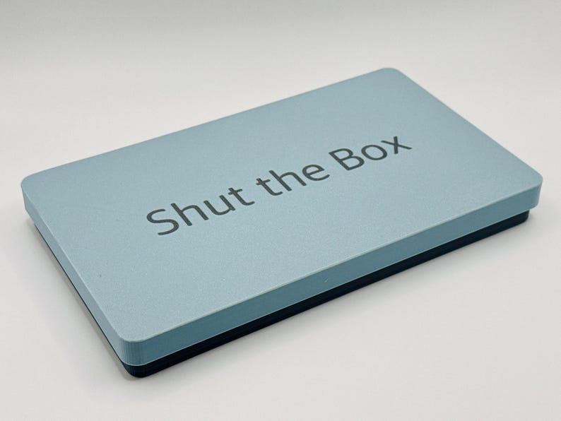 May include: A light blue box with the text "Shut the Box" printed on the top.