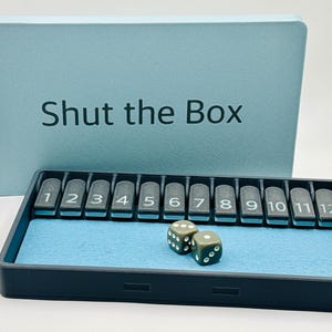 May include: A blue and black Shut the Box game with two dice. The game board has numbered tiles from 1 to 12.