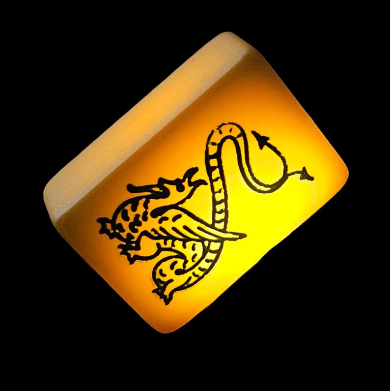 May include: A rectangular mahjong tile with a translucent yellow finish and a black engraved graphic of a dragon. The dragon is depicted in profile with a long, curved tail ending in a pointed tip, positioned centrally on the smooth surface.
