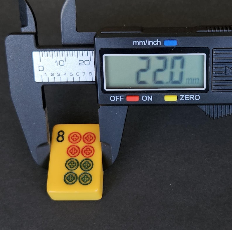 May include: A yellow mahjong tile featuring the number 8 and eight circular symbols in red and green, measured by a black digital caliper showing a width of 22.0 mm. The tile has a smooth, rectangular surface with rounded corners and clear markings.