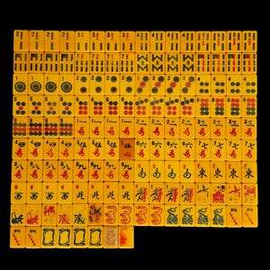 May include: A complete set of yellow mahjong tiles arranged in a grid on a black background. The tiles feature various engraved symbols, including bamboo sticks, circular patterns, Chinese characters, directional markers, dragons, and flower motifs.