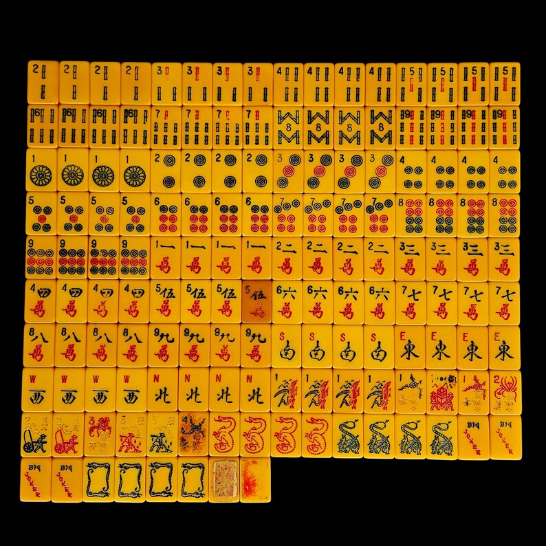 May include: A complete set of yellow mahjong tiles arranged in a grid on a black background. The tiles feature various engraved symbols, including bamboo sticks, circular patterns, Chinese characters, directional markers, dragons, and flower motifs.