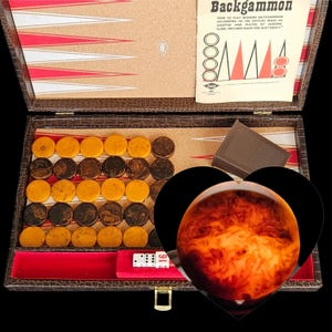 May include: A brown faux-leather backgammon set with a cork playing surface, red and white triangular points, and marbled yellow and dark brown checkers. Includes a rule booklet, dice, and a doubling cube, with a heart-shaped overlay graphic.