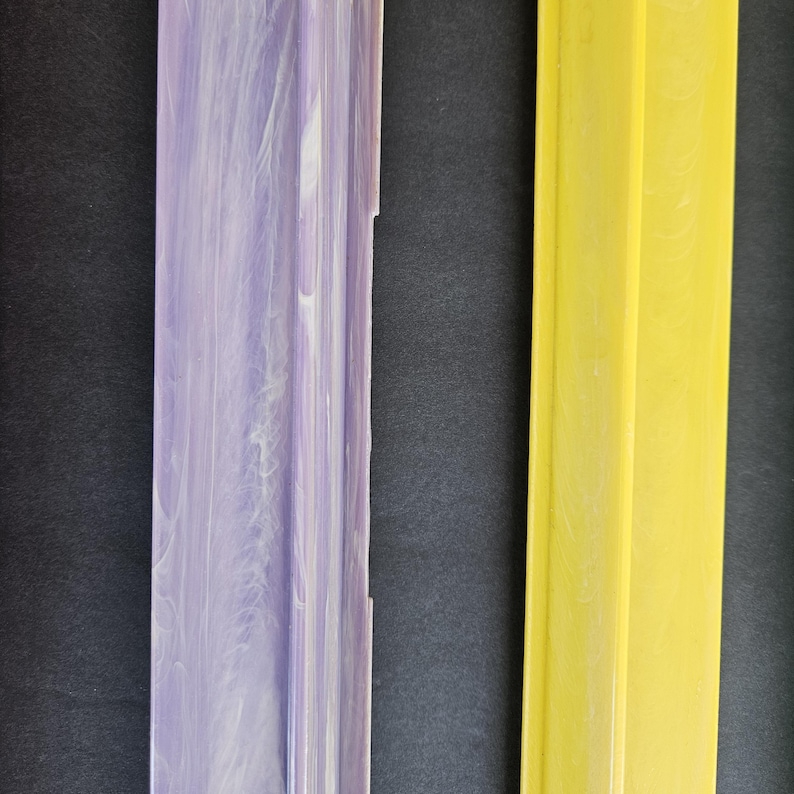May include: Two long, rectangular strips of material. The left strip features a marbled pattern of light purple and white. The right strip is a solid, bright yellow color. Both items have a raised, central ridge running vertically along their length.