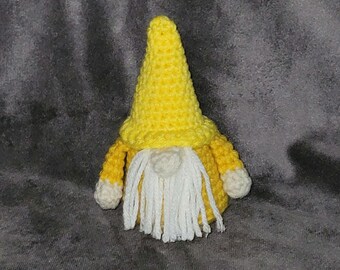Puede incluir: Un gnomo de ganchillo hecho a mano con un gorro puntiagudo amarillo y una chaqueta a juego. El gnomo tiene una barba blanca y pequeñas manos blancas. El gnomo mide aproximadamente 13 cm de alto.