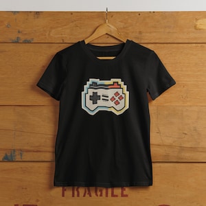 May include: Black t-shirt featuring a retro-style pixelated video game controller graphic in yellow, blue, red, and white.