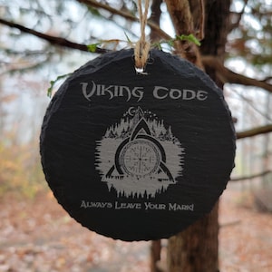 May include: A black slate ornament with a white design of a Viking symbol, a mountain, and trees. The text "Viking Code" and "Always Leave Your Mark!" is engraved on the ornament.