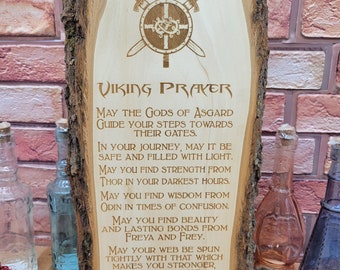 May include: A wooden plaque with a Viking prayer engraved on it. The prayer is about finding strength, wisdom, and beauty. The plaque is decorated with a shield and crossed swords.
