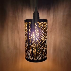 May include: A black metal pendant light with a cut-out design that allows light to shine through. The light is on and casting a warm glow.