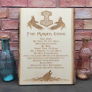 May include: A wooden sign with a carved image of a raven and a hammer. The sign has the text "The Raven Code" and a list of rules, including "Hail Odin, Be True to Thy Self, Seek Knowledge, Be Wise, Make Time to Play, Be a Friend to the Wolf, Do Not Fear Death, Find the Light Within the Darkness, Use Cunning and Trickery to Defeat Your Enemies, Soar High, Discover New Mysteries, Make Every Moment Magical."