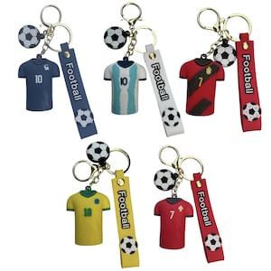 May include: Set of six soccer jersey keychains with a black and white soccer ball charm. Each keychain features a different soccer jersey with a number on the front and the word "Football" on a tag.