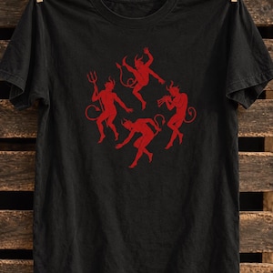 May include: A black short-sleeved t-shirt featuring a red graphic print of four dancing devil figures. One figure holds a trident, another plays a trumpet, and all have horns and tails. The design is centred on the chest of the garment.
