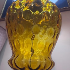 May include: A large, amber-colored glass lamp base featuring a bulbous, rounded shape with a textured surface of raised circular indentations. The glass is translucent, catching light to highlight the deep yellow-orange hue and the reflective, glossy finish of the material.
