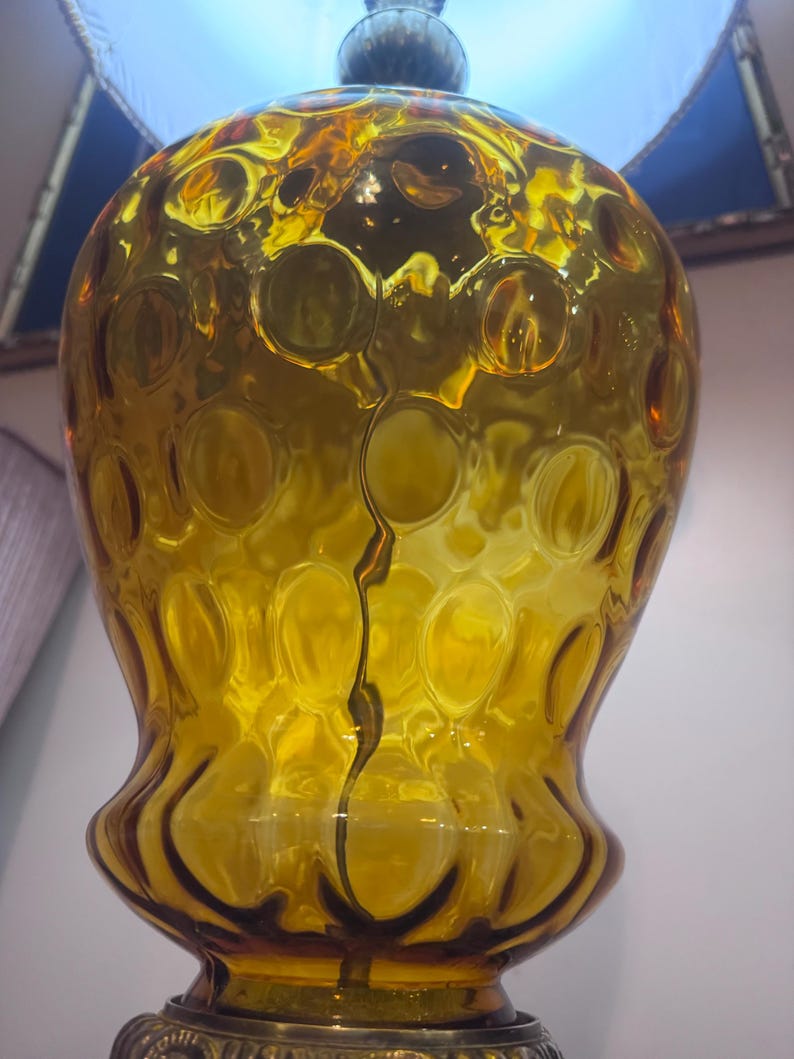 May include: A large, amber-colored glass lamp base featuring a bulbous, rounded shape with a textured surface of raised circular indentations. The glass is translucent, catching light to highlight the deep yellow-orange hue and the reflective, glossy finish of the material.