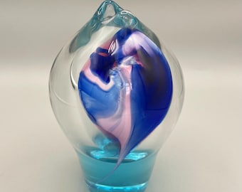 May include: A clear glass orb with a swirling blue, pink, and white design inside. The orb is sitting on a blue base.