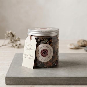 Peut inclure: Un bocal en plastique transparent rempli de pot-pourri séché, doté d'un couvercle argenté et d'une étiquette ronde portant l'inscription Officina del Pot Pourri Home Fragrances. Une étiquette en papier beige indique Foresta Aromatica Abete, Spezie, Pino e Agrumi.
