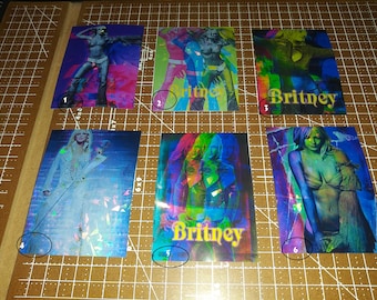 Könnte beinhalten: Sechs holografische Sammelkarten mit einem Popstar, auf denen der Name "Britney" steht. Die Karten sind in verschiedenen Farben, darunter Blau, Grün, Pink und Lila.