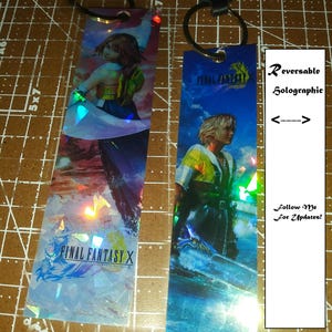 May include: Two reversible holographic keychains featuring characters from Final Fantasy X. One keychain shows a female character, the other a male character. Each keychain has a black strap and a metal ring. The text "Final Fantasy X" is visible.