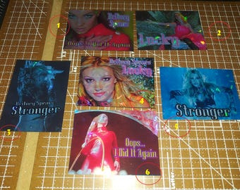 May include: Six rectangular trading cards featuring Britney Spears with holographic finishes. The cards display images from the music videos for Oops... I Did It Again, Lucky, and Stronger, with the corresponding song titles and artist name printed on each.