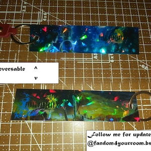 May include: Reversible keychain featuring Final Fantasy artwork. The keychain has a rectangular design with a metal ring and a red leather strap. The text "Final Fantasy" is visible on one side. The background has a colorful, iridescent design.