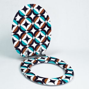 Peut inclure: Abattant de toilette ovale avec un motif géométrique rétro. Le motif présente des cercles superposés en turquoise, marron, noir et blanc. Le siège est ouvert, révélant l'intérieur, et est fixé aux charnières.