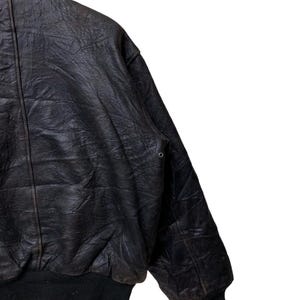 May include: A vintage black leather bomber jacket with a ribbed hem and cuffs. The jacket has a classic collar and a slightly distressed appearance, suggesting it's been well-worn. The leather has a textured surface.