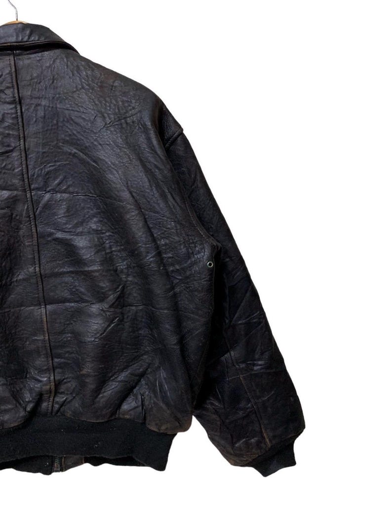 May include: A vintage black leather bomber jacket with a ribbed hem and cuffs. The jacket has a classic collar and a slightly distressed appearance, suggesting it's been well-worn. The leather has a textured surface.