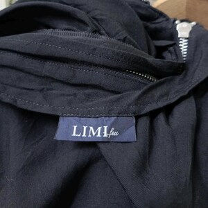 May include: Close-up of a dark navy blue garment with a zipper and a label that reads "LIMI feu" in white lettering. The fabric appears to be a soft, woven material. The zipper is silver.