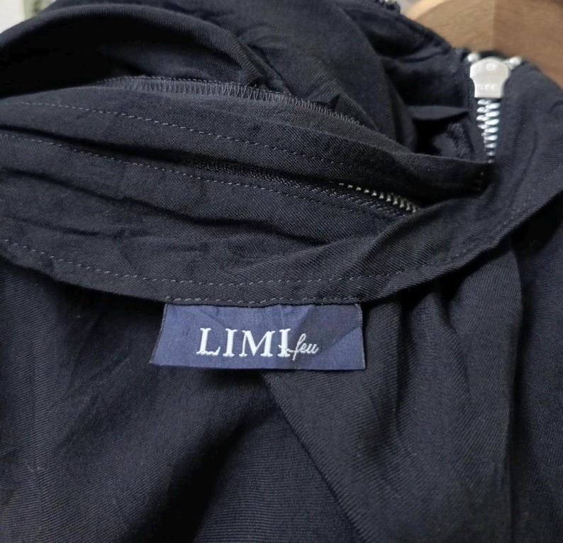 May include: Close-up of a dark navy blue garment with a zipper and a label that reads "LIMI feu" in white lettering. The fabric appears to be a soft, woven material. The zipper is silver.