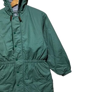Pu&ograve; includere: Giacca con cappuccio verde con vita con coulisse e chiusura con bottoni. La giacca ha un cappuccio foderato in pile grigio e due tasche anteriori. La giacca &egrave; realizzata in un materiale leggero e sembra essere vintage.