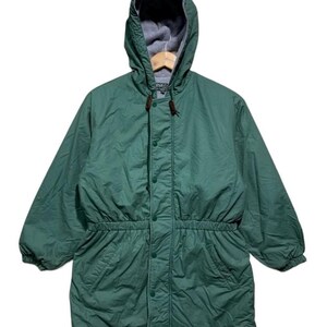 Pu&ograve; includere: Giacca verde con cappuccio, vita con coulisse e chiusura con bottoni. La giacca ha una fodera in pile grigio nel cappuccio ed &egrave; appesa a una gruccia di legno. La giacca ha due tasche anteriori.