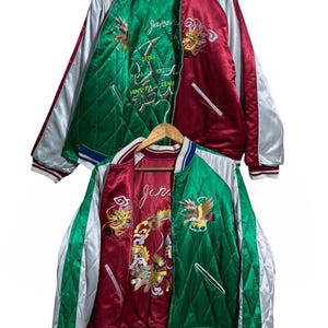 Puede incluir: Dos chaquetas bomber reversibles de satén. Una es roja y verde con diseños bordados y la palabra "Japan". La otra es verde y roja con diseños bordados y la palabra "Japan". Ambas chaquetas tienen forro acolchado y una raya plateada en las mangas.