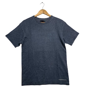 May include: A dark gray t-shirt with short sleeves, hanging from a wooden hanger. The shirt has a crew neck and a small logo on the lower right side. The fabric appears to be a soft, comfortable material.