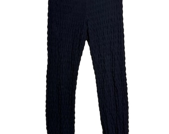 Puede incluir: Pantalones de punto negro con un patrón texturizado de canalé vertical en toda la tela. La prenda tiene una cintura ajustada y piernas cónicas que terminan en puños acanalados. Una pequeña etiqueta blanca de marca está unida a la cintura interior.