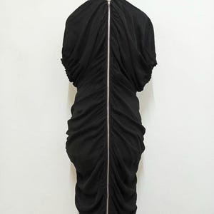 May include: A white ceramic mug with a black handle and the text "But First, Coffee" in a bold, black font. The mug is set against a neutral background, highlighting its simple design.