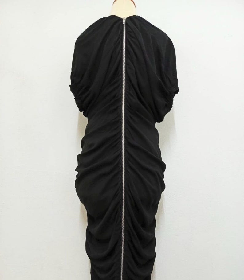 May include: A white ceramic mug with a black handle and the text "But First, Coffee" in a bold, black font. The mug is set against a neutral background, highlighting its simple design.