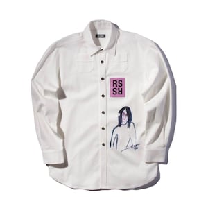Peut inclure: Chemise blanche à manches longues avec col et boutons noirs. Elle présente un petit carré rose avec les lettres "RS" blanches et un dessin d'une personne en noir et bleu.