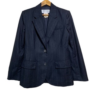 May include: A navy blue blazer with subtle pinstripes, featuring a two-button closure and two front pockets. The blazer is hanging on a wooden hanger. The label reads "Yves Saint Laurent".