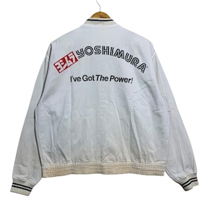May include: White bomber jacket with the text "YOSHIMURA" in black and red, and the phrase "I've Got The Power!" The jacket has black and white striped cuffs and collar.