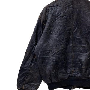 May include: A vintage black leather bomber jacket with a classic collar and ribbed cuffs and hem. The jacket shows signs of wear, with a distressed appearance. The jacket is hanging on a wooden hanger.