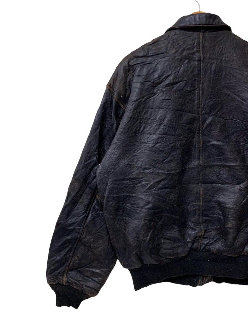 May include: A vintage black leather bomber jacket with a classic collar and ribbed cuffs and hem. The jacket shows signs of wear, with a distressed appearance. The jacket is hanging on a wooden hanger.