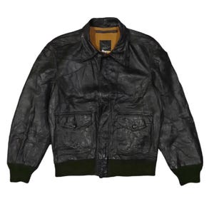 May include: Black leather jacket with a collared neckline, two front pockets, and a green ribbed hem and cuffs. The jacket has a classic bomber style and a vintage aesthetic.
